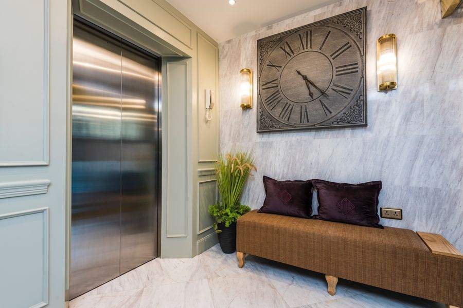 The lift lobby at The Elite Thong Lor 25, with a wall clock and panelled walls