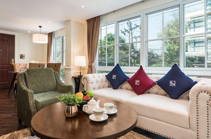 The living room at The Elite Thong Lor 25, with buttoned Chesterfield sofas, panelled walls, herringbone timber floor and full height windows