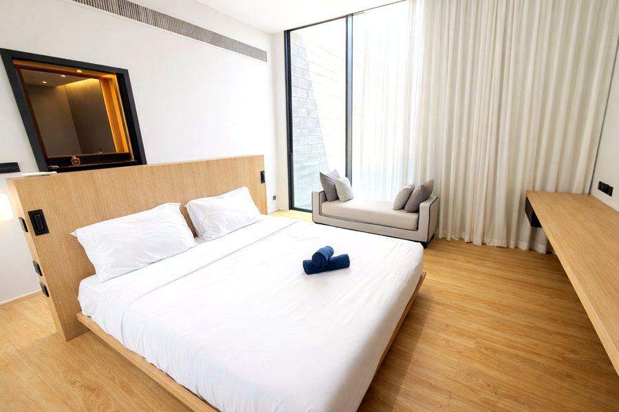 The main bedroom at The Elite @ Pattaya with a king bed, an oak headboard and a window seat under full height glass